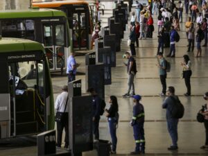 Passageiros e ônibus em terminal de transporte coletivo urbano