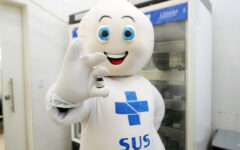Personagem do SUS segura frasco de vacina em unidade de saúde