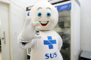 Personagem do SUS segura frasco de vacina em unidade de saúde