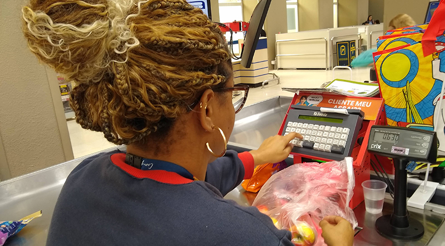 Trabalhadora registra produtos no caixa de estabelecimento comercial