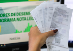 Consumidora segura notas fiscais diante da página do programa Nota Legal