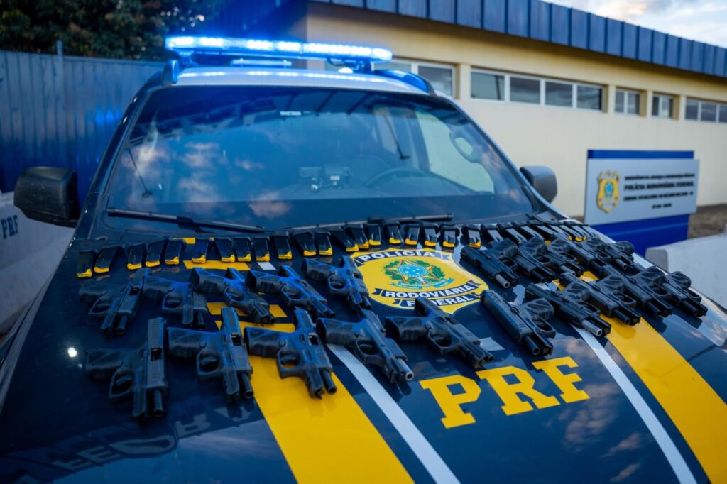 Pistolas e carregadores apreendidos estão expostos sobre uma viatura da PRF
