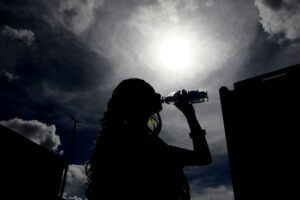 Pessoa bebe água sob sol forte durante período de tempo seco