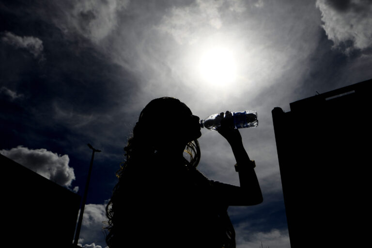 Pessoa bebe água sob sol forte durante período de tempo seco