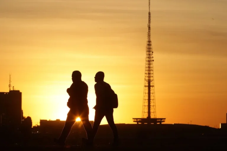 Pessoas caminham em Brasília sob o sol forte no fim da tarde