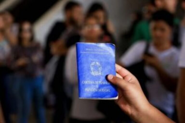 Pessoa segura uma carteira de trabalho diante de trabalhadores