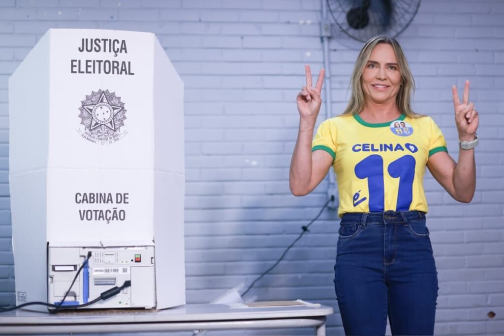Celina Leão faz gesto de vitória ao lado de uma cabine de votação