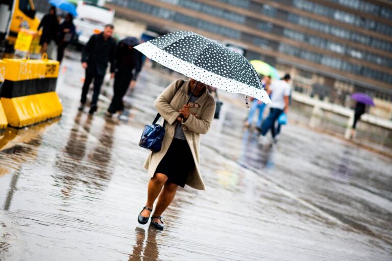 Pedestre atravessa área aberta de Brasília sob chuva e segurando guarda-chuva