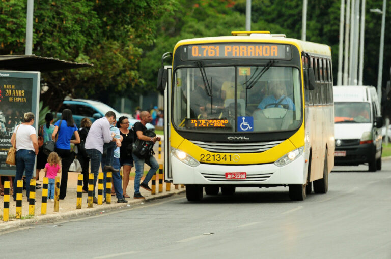 Ônibus do transporte público do DF circula em via próxima a uma parada com passageiros